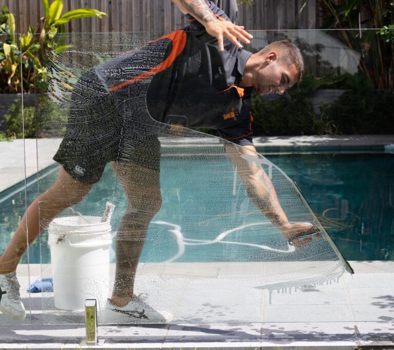 worker leaning over to clean pool glass with a squeegee
